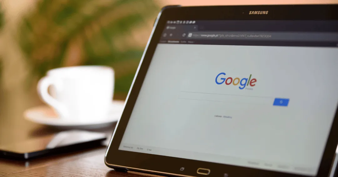 Tablet on a table showing the Google search home page beside a coffee cup