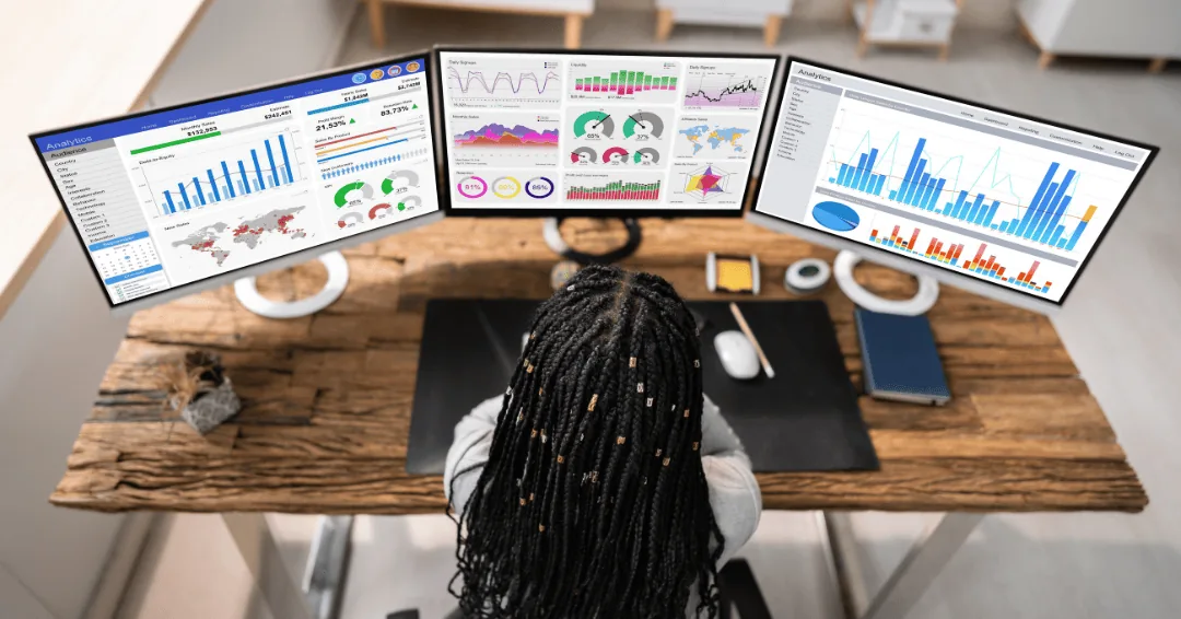 Woman analyzing marketing data dashboards across three computer monitors