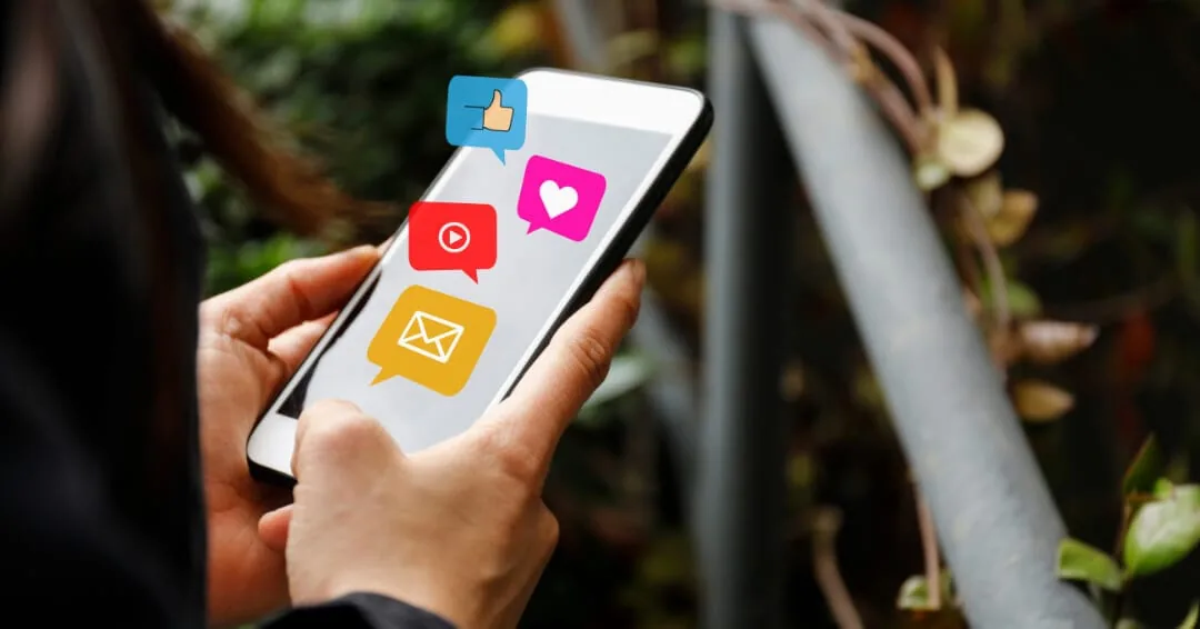 Hands holding a smartphone with like, heart, video and message notification icons popping out